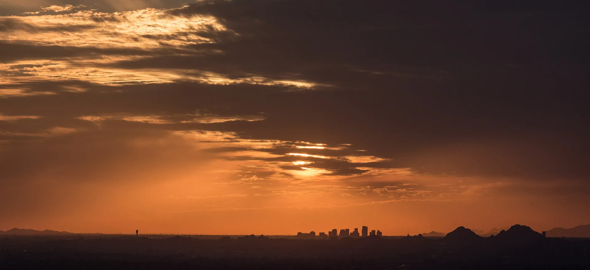 Downtown Phoenix skyline silhouetted under an orange sunset sky