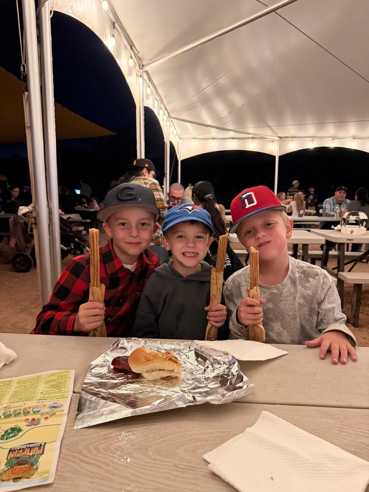 Three churros held up under the string-lit dinner tent, hot dog on the table