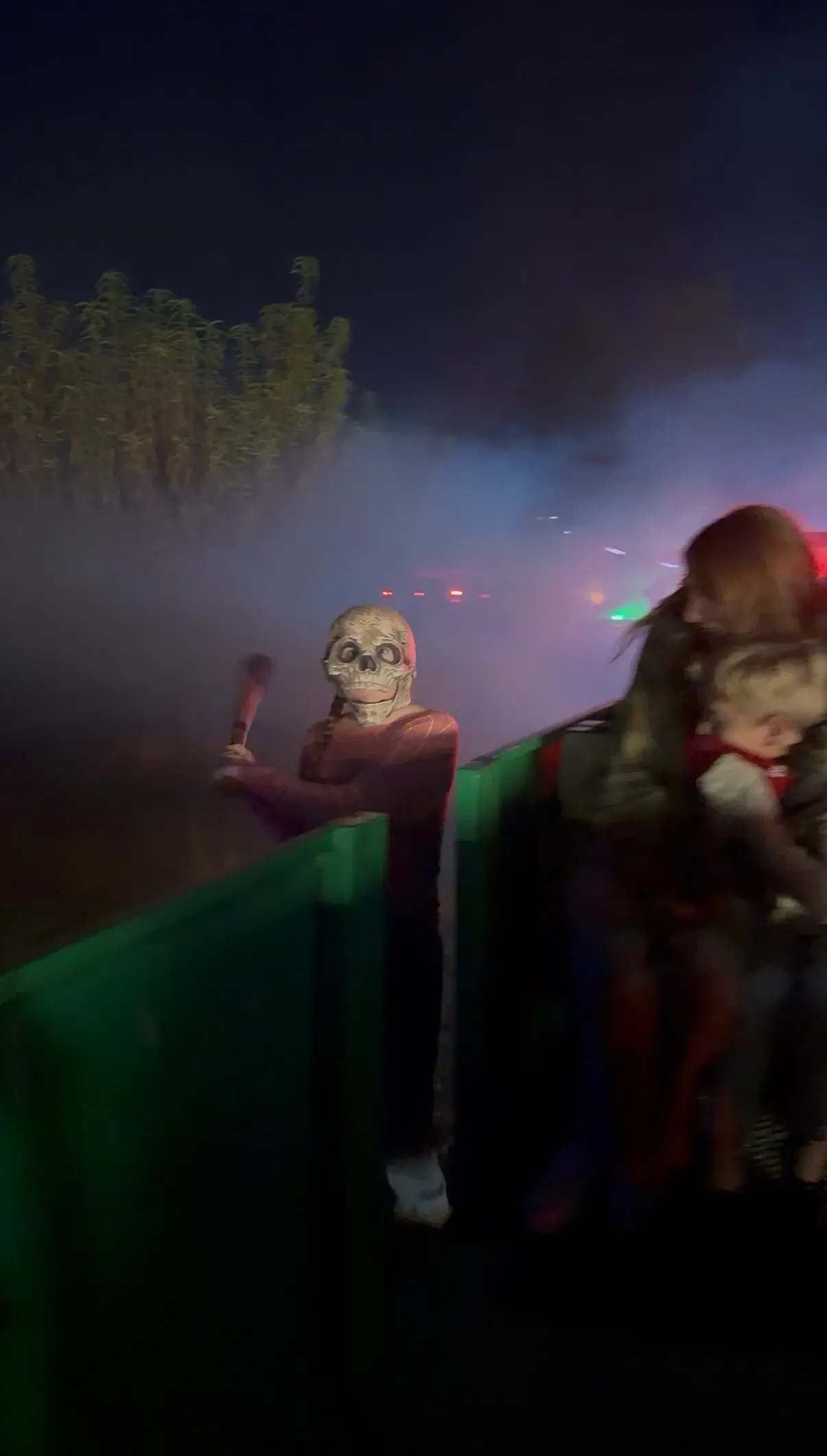 A skeleton scare actor with a mallet emerging from the fog alongside the moving spooky train at night