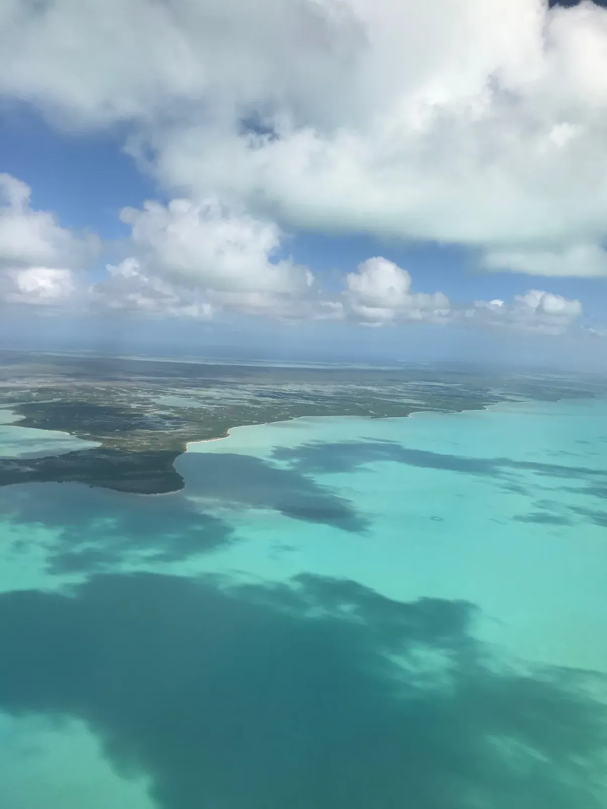 The Caicos Banks from the plane: turquoise water, dark reef patches and cloud shadows